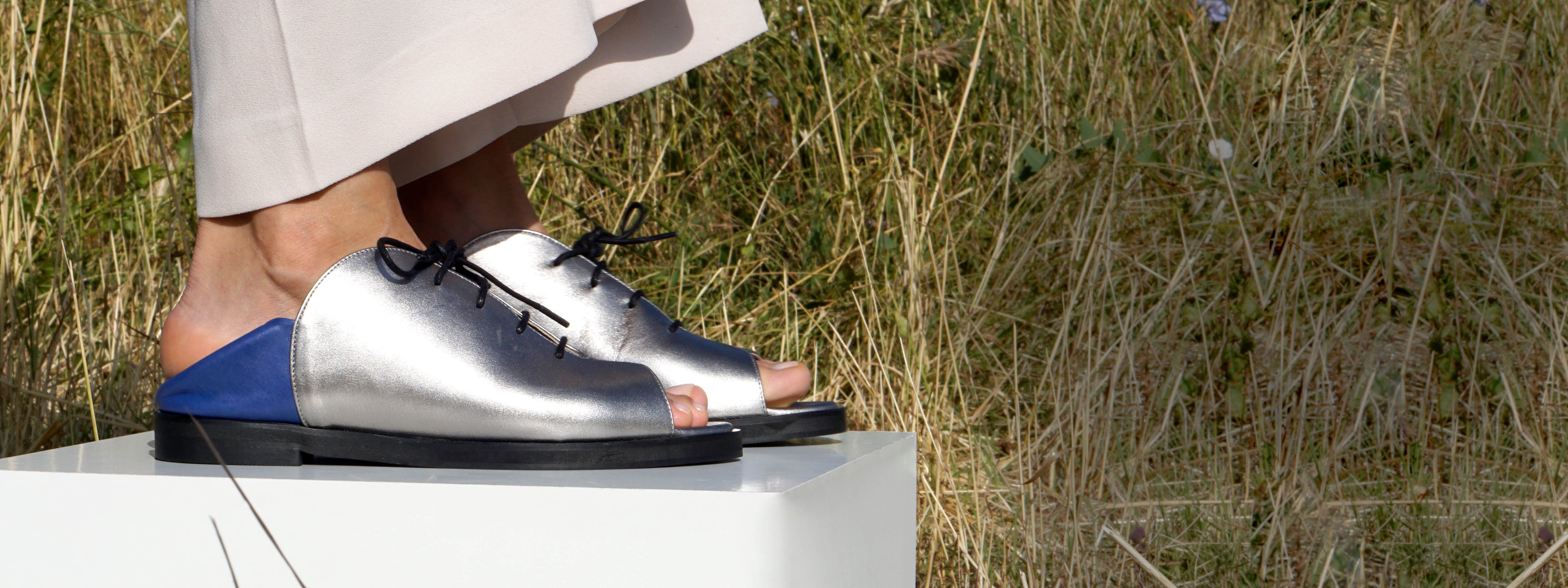 Silver shoes with blue soles worn by a person on a white platform with grass in the background