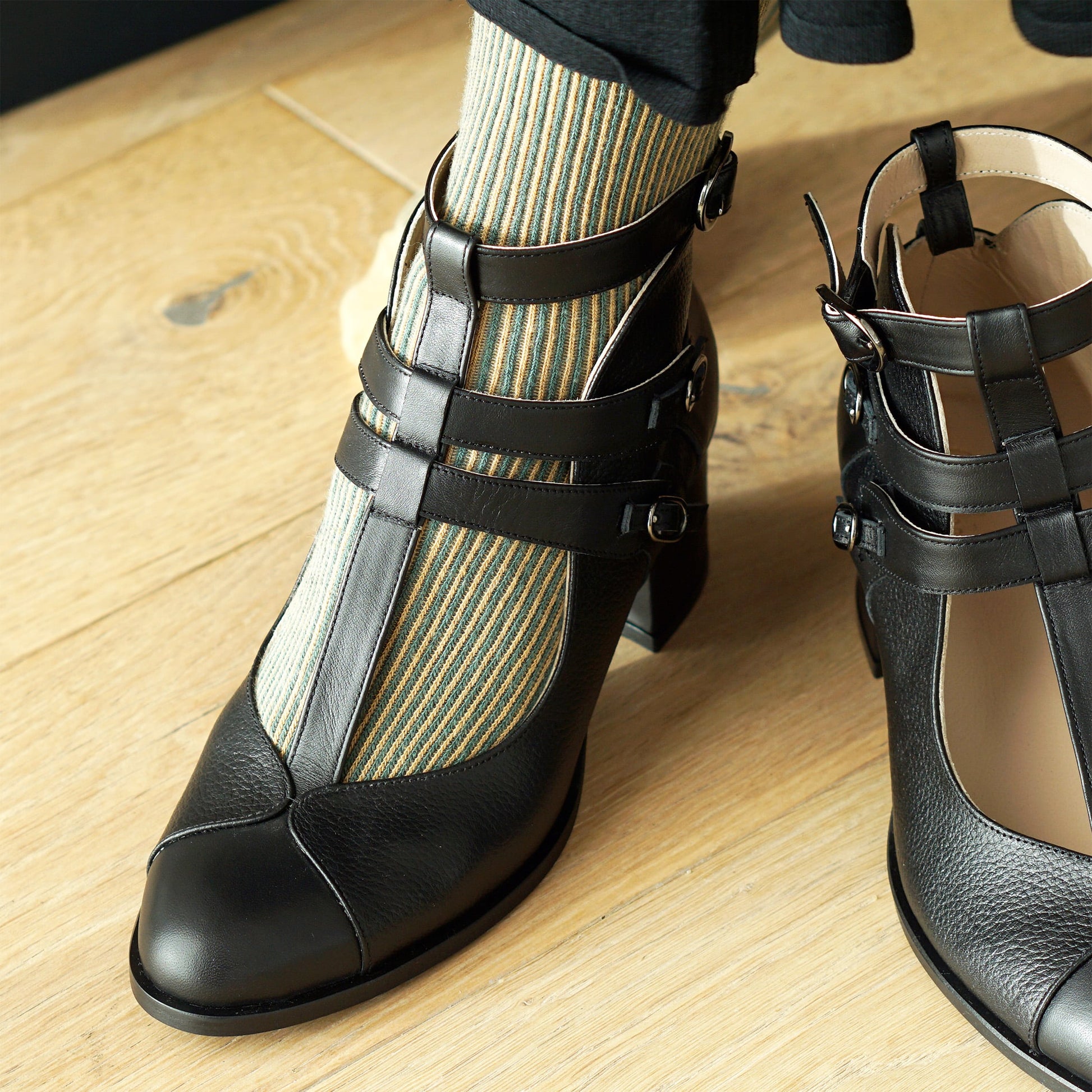 Black strappy shoes worn with striped socks on a wooden floor