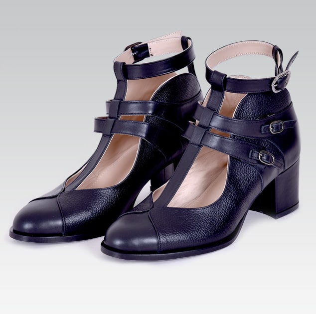 Pair of black leather shoes with strap details on a light gray background